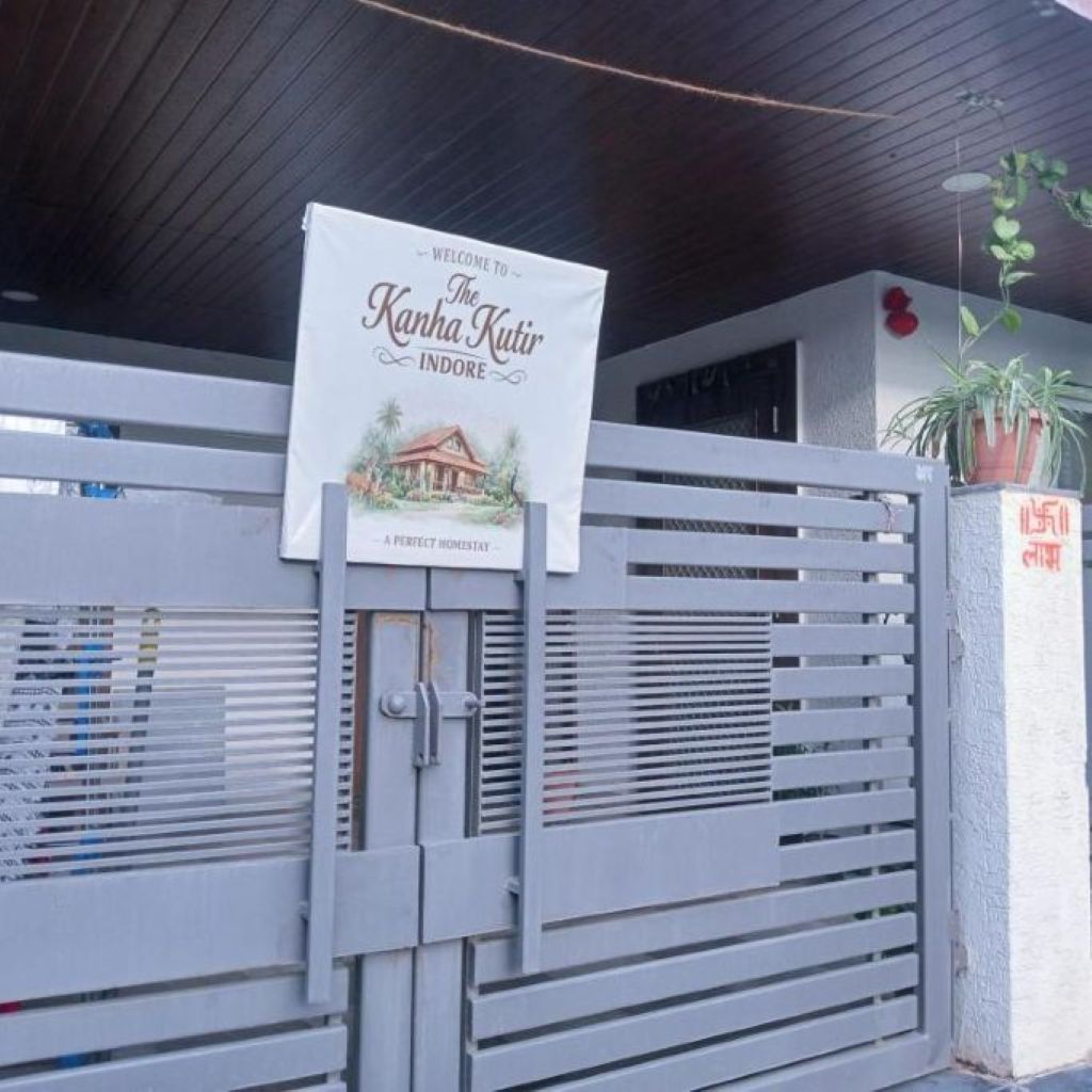 A gated entrance with a welcome sign for 'The Kanha Kutir Indore' and a small house illustration.