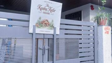 A gated entrance with a welcome sign for 'The Kanha Kutir Indore' and a small house illustration.