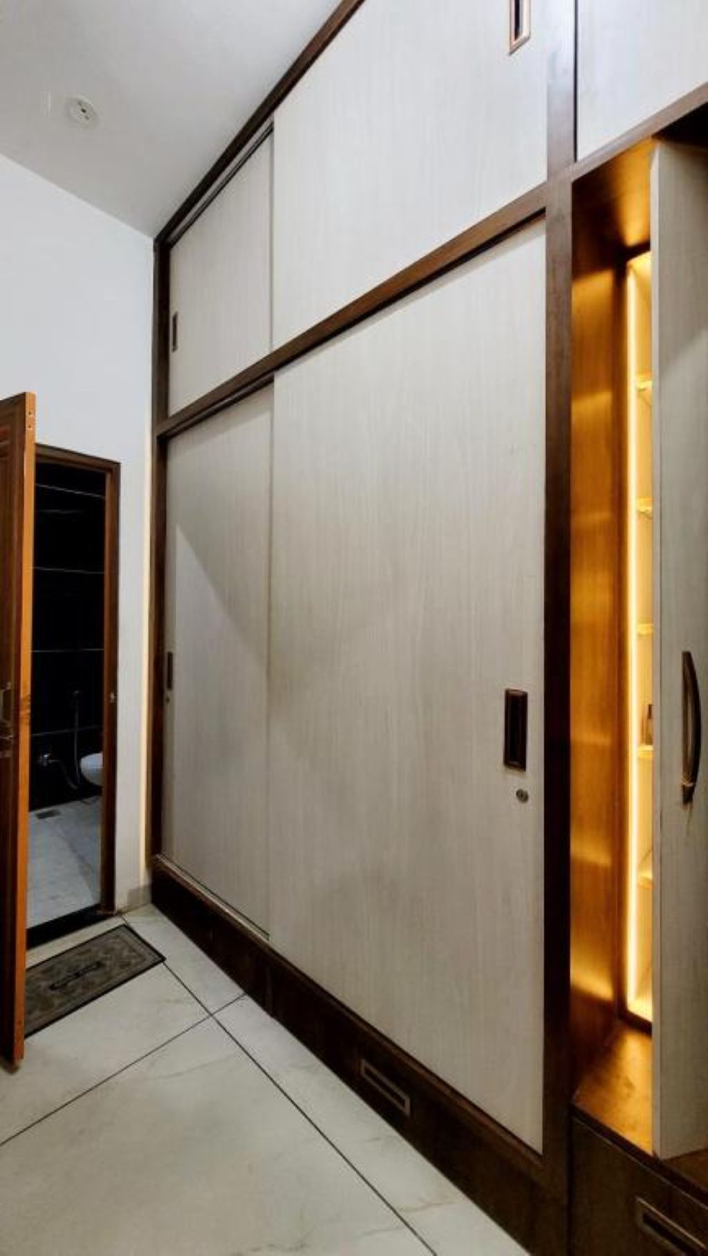 A room with a sliding door, a tiled floor, and a wall with a recessed lighting feature.