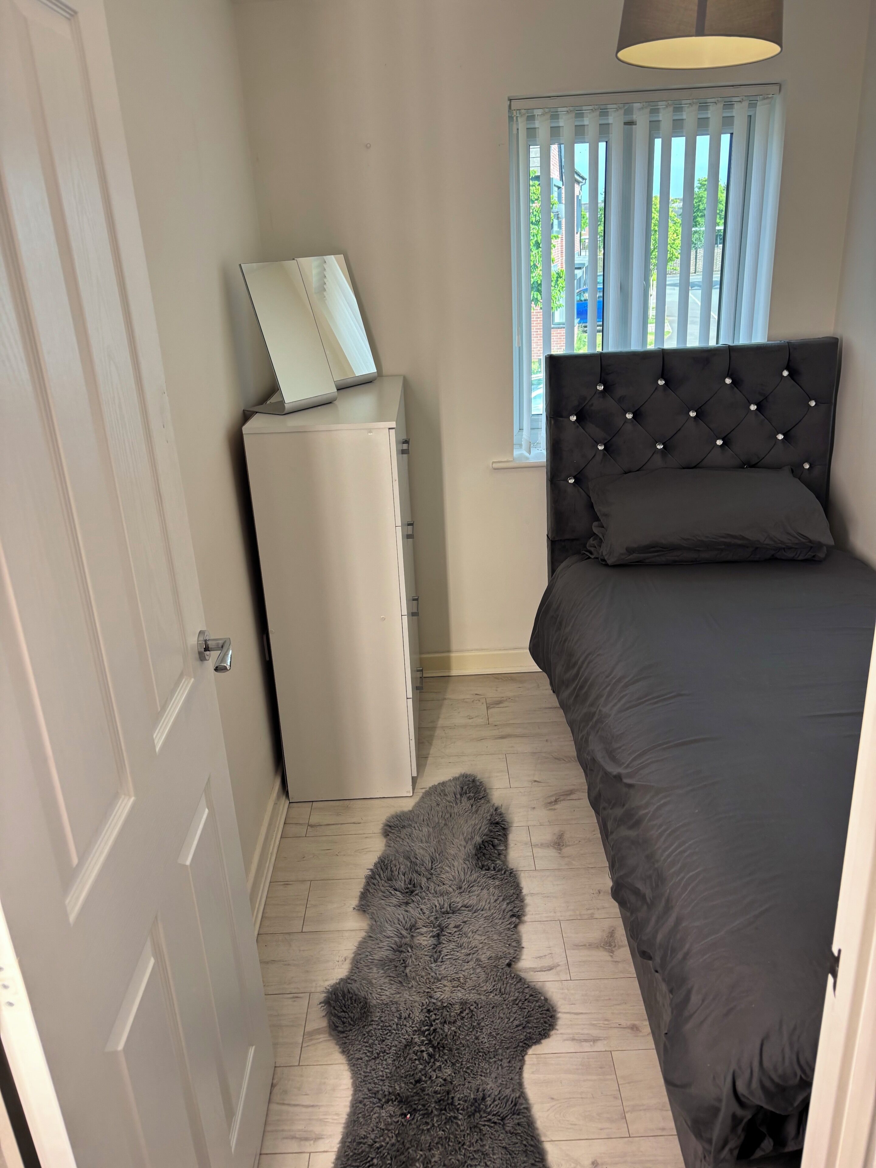 A bedroom with a bed, a wardrobe, a window with blinds, and a rug.