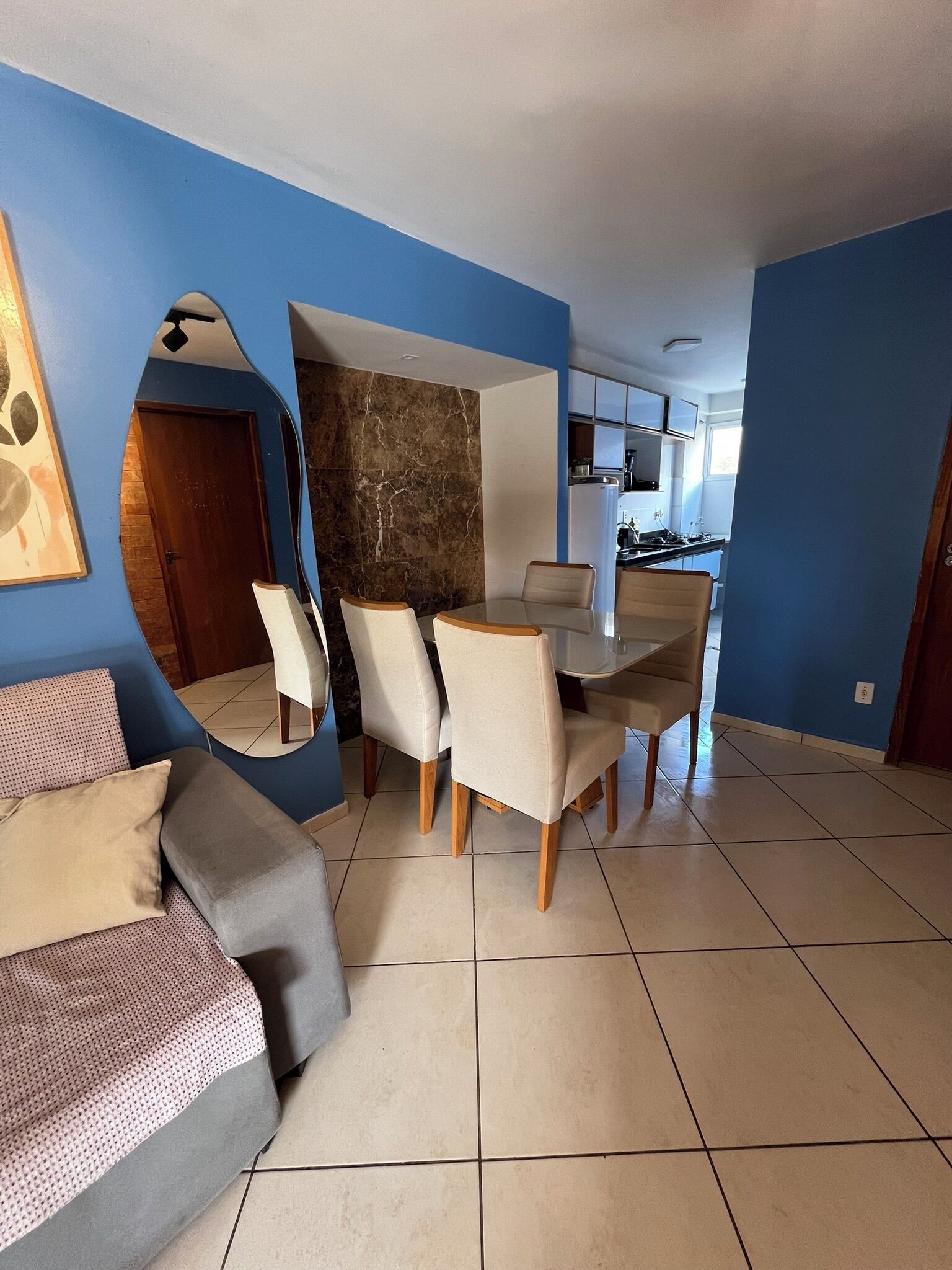 Un comedor con una mesa y sillas, una cocina al fondo y una sala de estar con un sofá y un espejo.