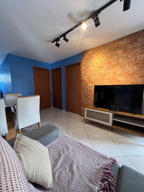 Una sala de estar con televisor de pantalla plana, un sofá, una mesa de centro y una pared decorada con ladrillos.