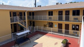 Un motel de dos pisos con un patio central, mobiliario exterior y un área de balcón amurallada.