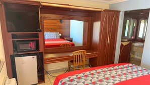 A compact hotel room with a bed, a desk, a chair, a small refrigerator, a microwave, and a mirror. - LISA MOTEL (Lake Worth Beach)
