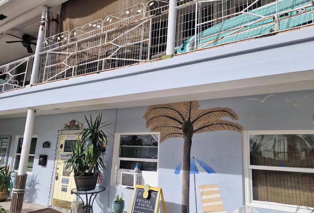 A building with a balcony, a palm tree mural, and a sign for cottage rentals.