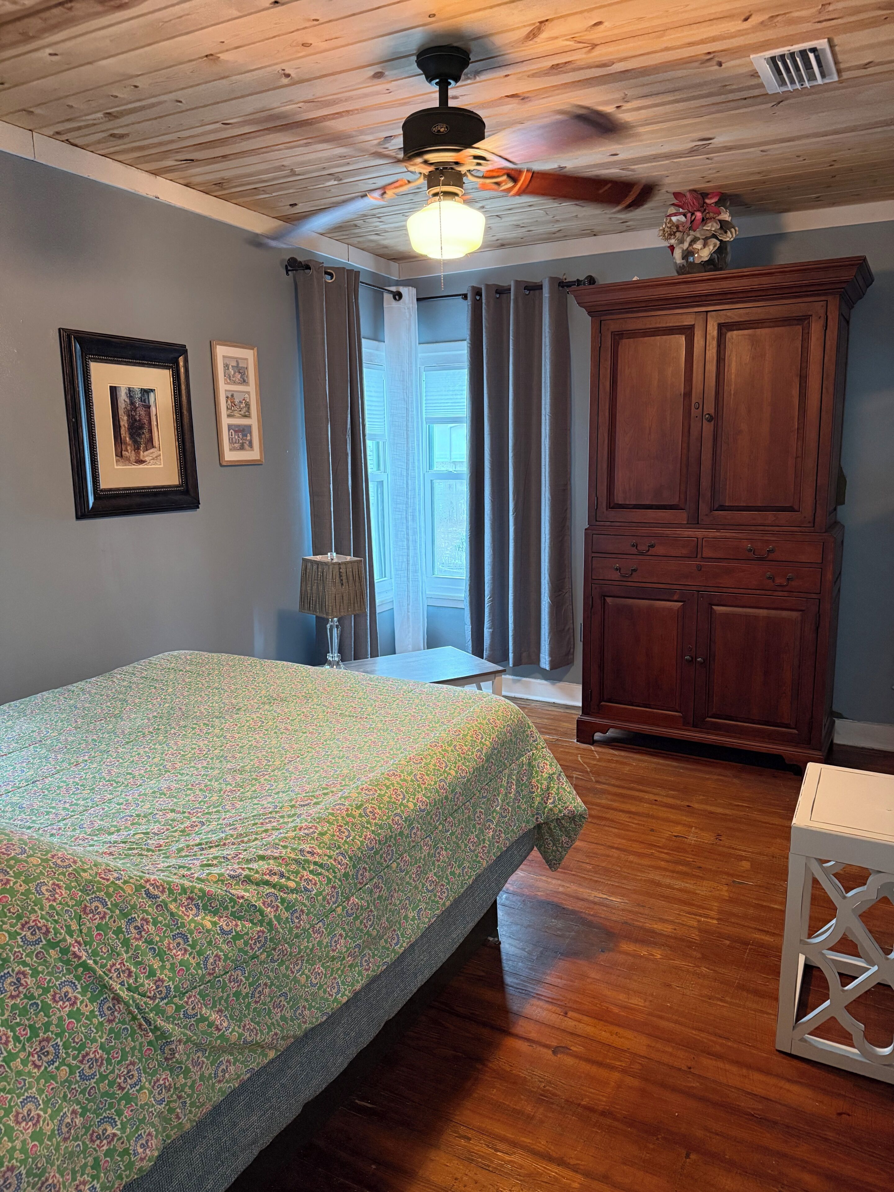A room with a bed, wooden wardrobe, and a ceiling fan.