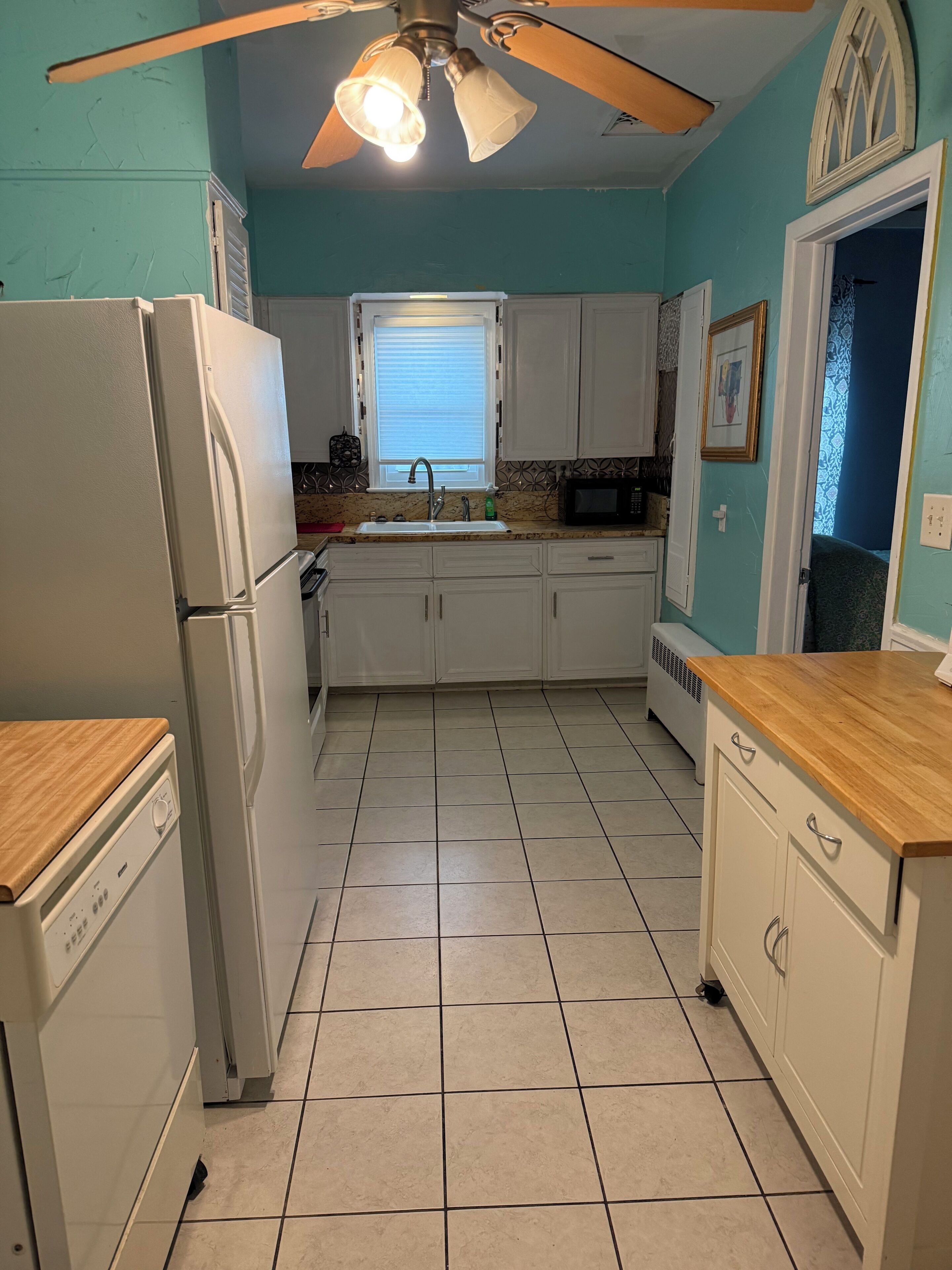 A kitchen with white cabinets, a refrigerator, a microwave, and a ceiling fan.