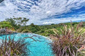 Ein klares, blaues Schwimmbecken, umgeben von üppiger Vegetation und einer Bergkulisse.