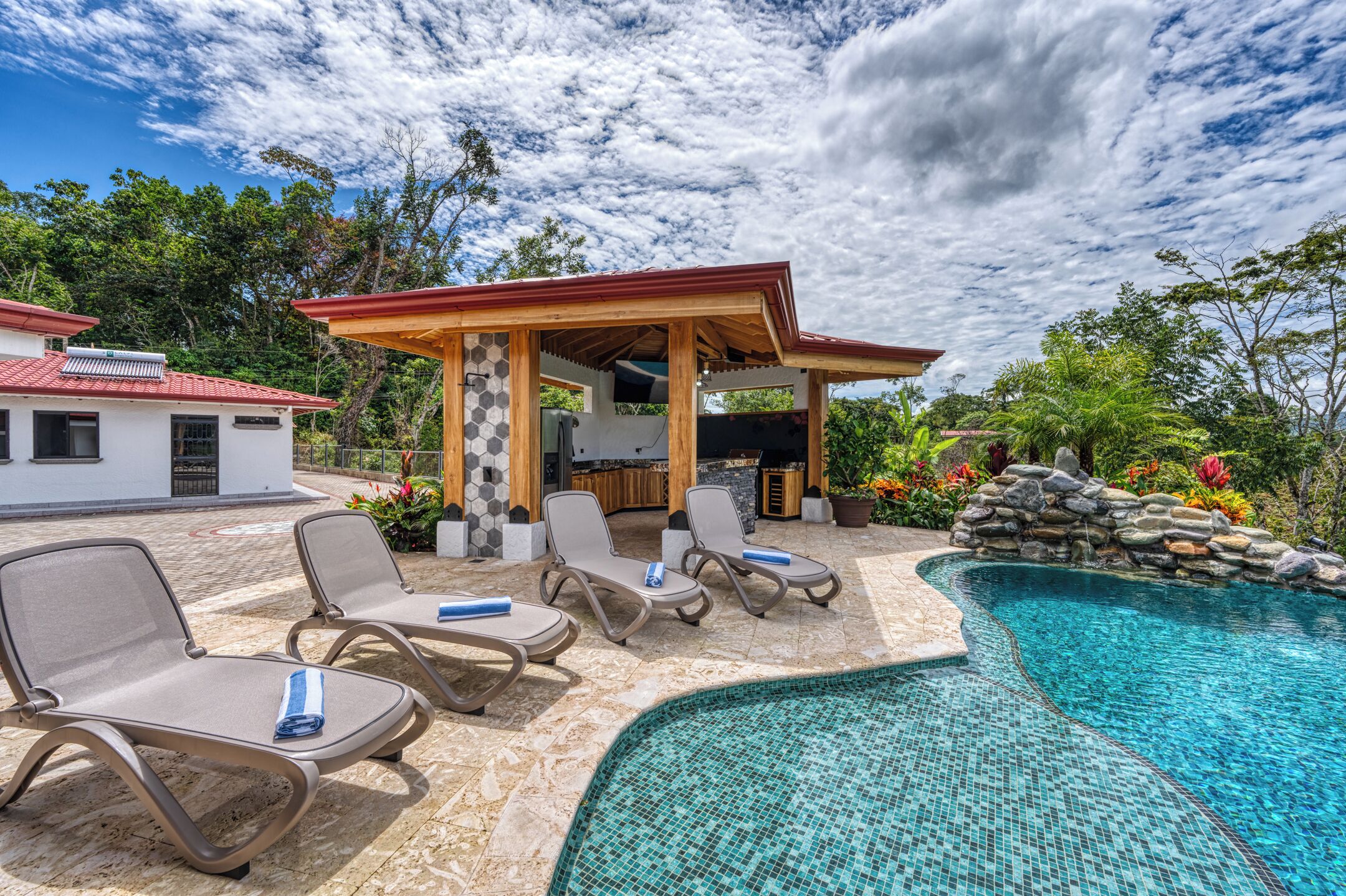 Un espace aménagé au bord de la piscine, avec des chaises longues et un espace barbecue couvert.