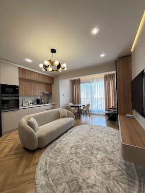 Een moderne woonkamer met een bank, een eettafel met stoelen, een keuken met inbouwapparatuur en een televisie.