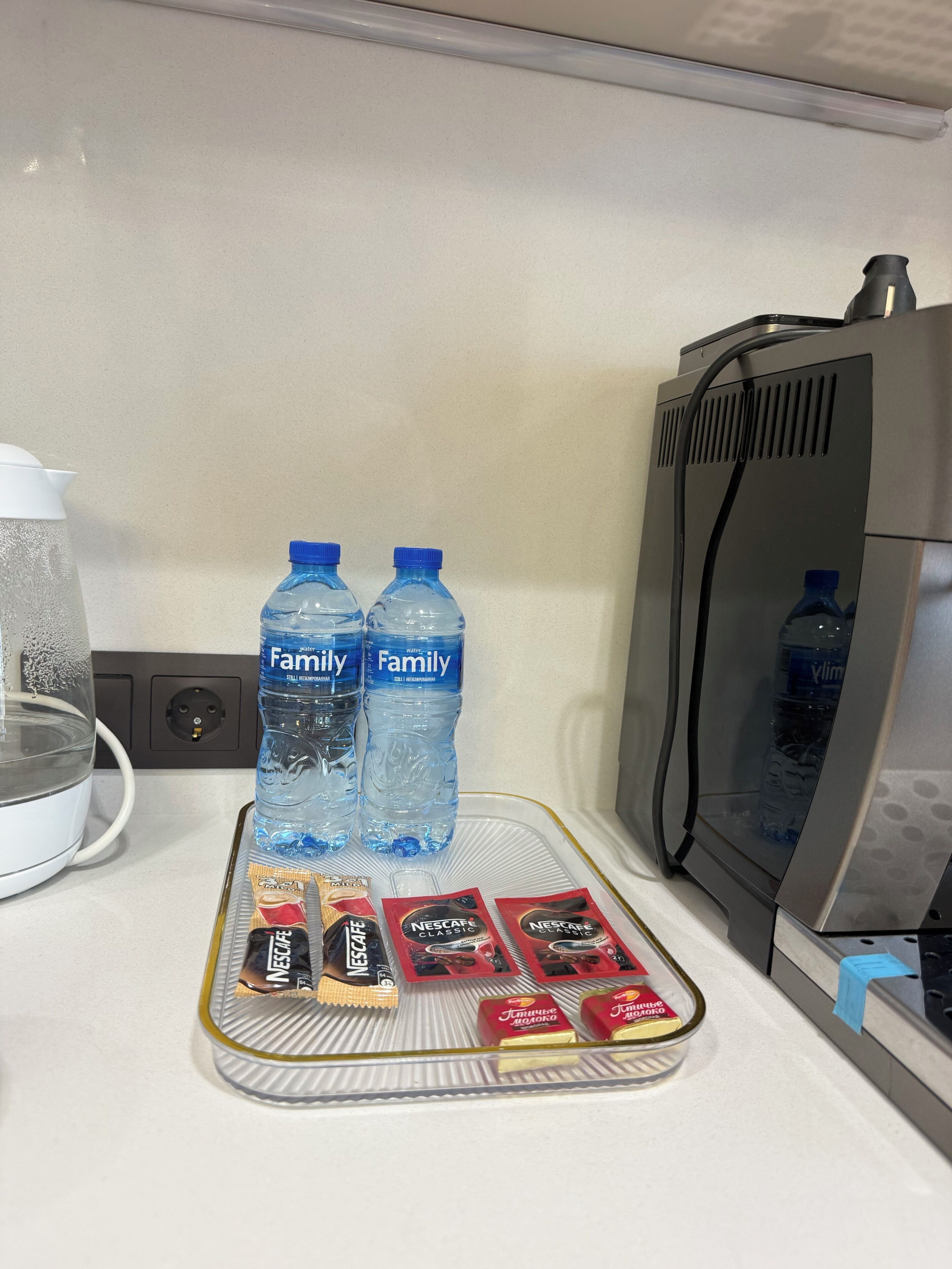 A kitchen counter with two water bottles, a coffee maker, and several packets of instant coffee.