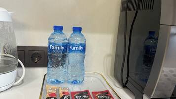 A kitchen counter with two water bottles, a coffee maker, and several packets of instant coffee.