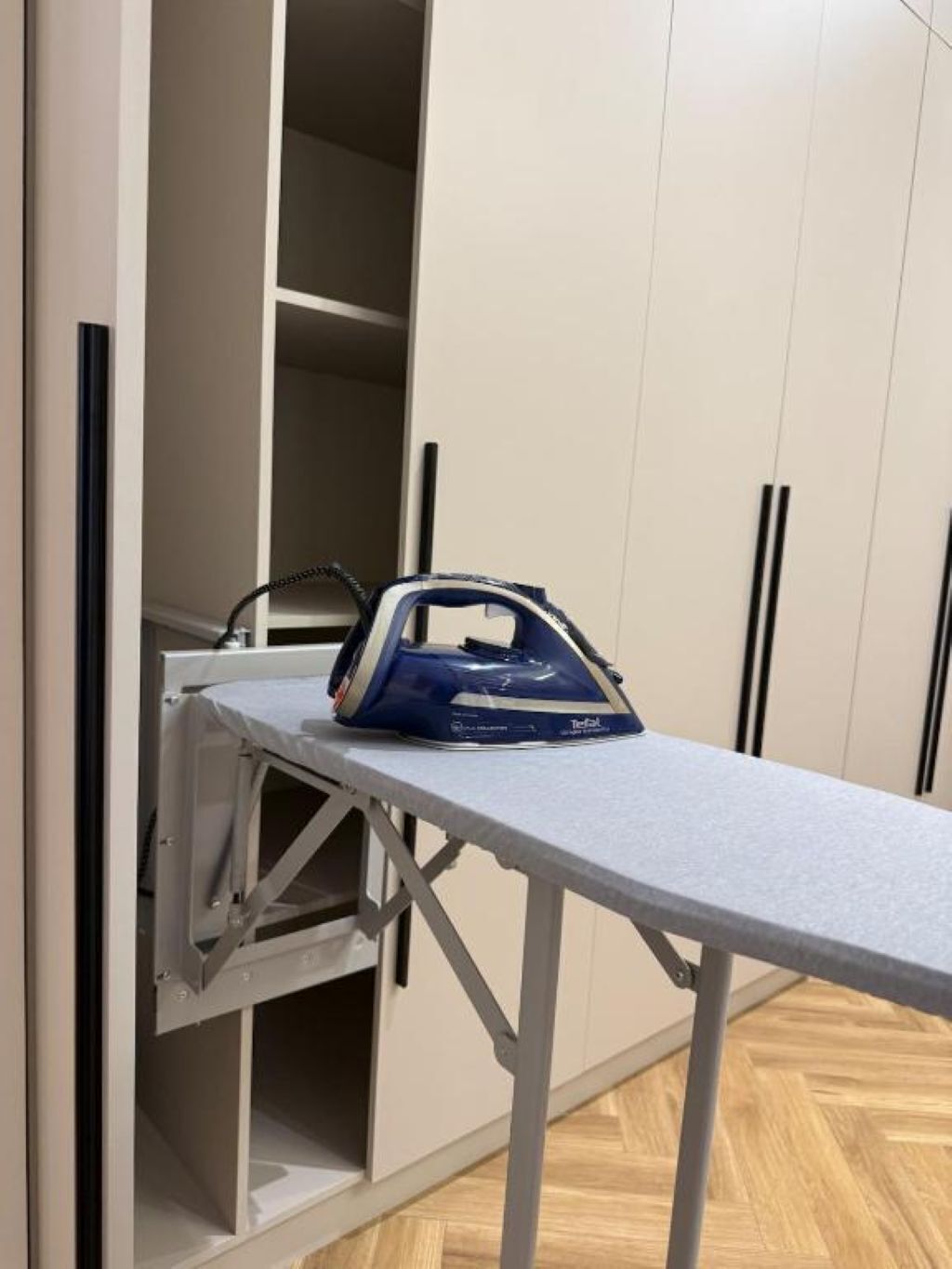 A room with a built-in ironing station and a wardrobe with black handles.