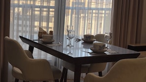 Een eetgedeelte met een tafel gedekt voor twee personen, stoelen en een uitzicht door dunne gordijnen.