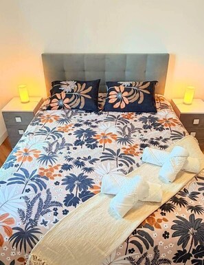 A bed with a floral bedspread, two pillows, and a tray with towels. - Madeira Sea Escape by Stayguest (Caniço)
