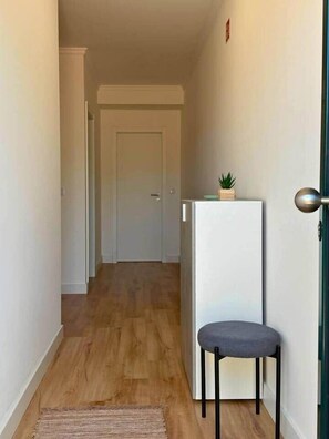 A hallway with a wooden floor, a white door at the end, and a small table with a chair and a plant on top. - Madeira Sea Escape by Stayguest (Caniço)