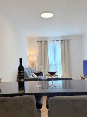 A modern living room with a dining area, a sofa, a TV, and a table with a bottle and glasses. - Madeira Sea Escape by Stayguest (Caniço)