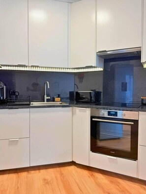 A modern kitchen with white cabinets, a stainless steel oven, and a black countertop. - Madeira Sea Escape by Stayguest (Caniço)