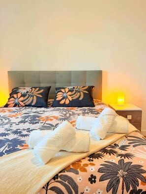 Ein ordentlich bezogenes Bett mit Blumenmuster, zwei Kissen und einer Nachttischlampe.