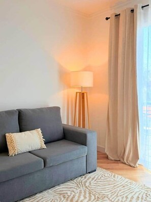 A living room with a grey sofa, a floor lamp, and a window with curtains. - Madeira Sea Escape by Stayguest (Caniço)