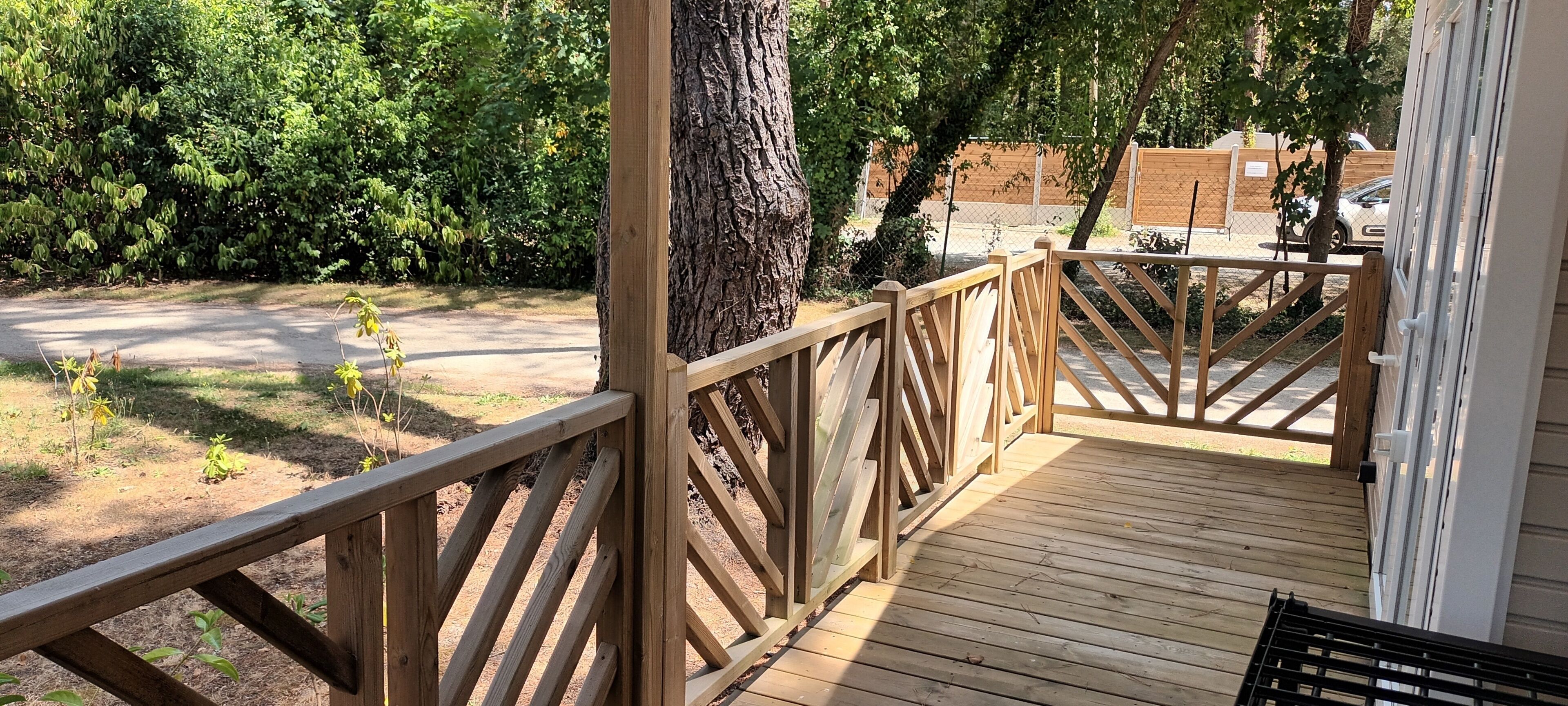 Eine Holzterrasse mit Geländer, umgeben von Bäumen und einem Zaun.