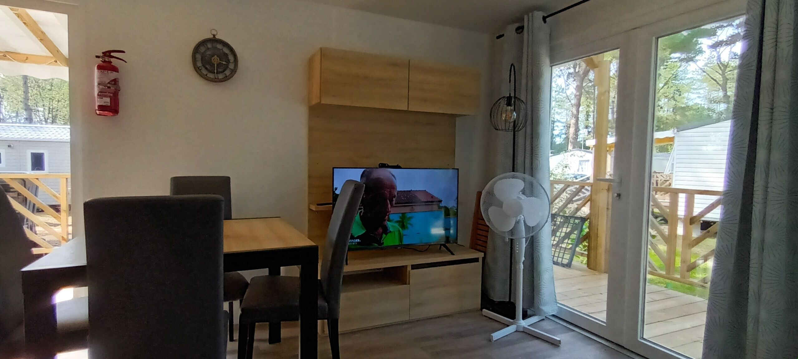 Una sala de estar con una televisión, un ventilador y un extintor en la pared.