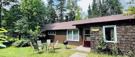 A rustic cabin with a red door, a small porch, and a grill.