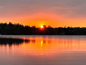 Ein Sonnenuntergang über einem ruhigen See mit bewaldeter Uferlinie.