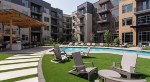 A modern apartment complex with a swimming pool, outdoor seating, and a covered patio area.