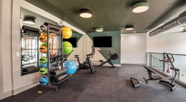 A gym with exercise equipment, a wall-mounted TV, and a staircase.