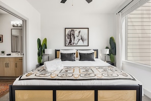 A modern bedroom with a large bed, a bedside table, a mirror, and a framed picture on the wall.