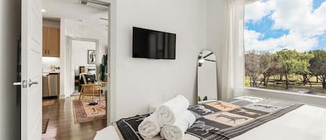 Un dormitorio con cama, televisor, ventana con vistas y puerta que da a un baño.