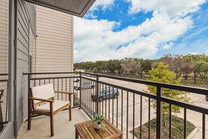A balcony with a chair and a small table, overlooking a parking area and trees. - Spacious 2BR Home with Everyday Comforts (Austin)