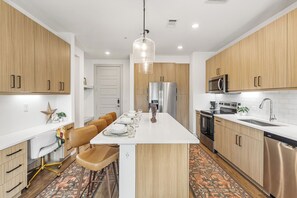 A modern kitchen with wooden cabinets, stainless steel appliances, and a central island with seating. - Spacious 2BR Home with Everyday Comforts (Austin)