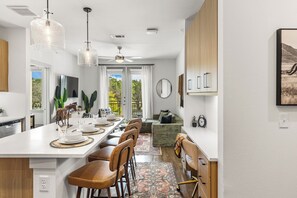 A modern kitchen with a large island, bar stools, and a dining area with a view of the outdoors. - Spacious 2BR Home with Everyday Comforts (Austin)