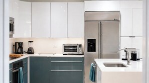 A modern kitchen with white cabinets, a stainless steel refrigerator, a built-in oven, a coffee maker, and a toaster. - Luxury Villa | Casa WED | Bahia Beach PR (Rio Grande)