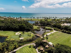 A golf course with water hazards, palm trees, and a view of the ocean. - Luxury Villa | Casa WED | Bahia Beach PR (Rio Grande)
