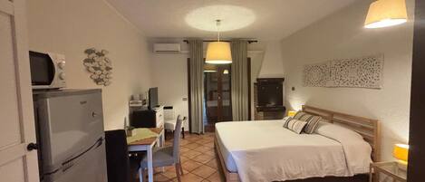 A compact hotel room with a bed, desk, chair, refrigerator, and a television.