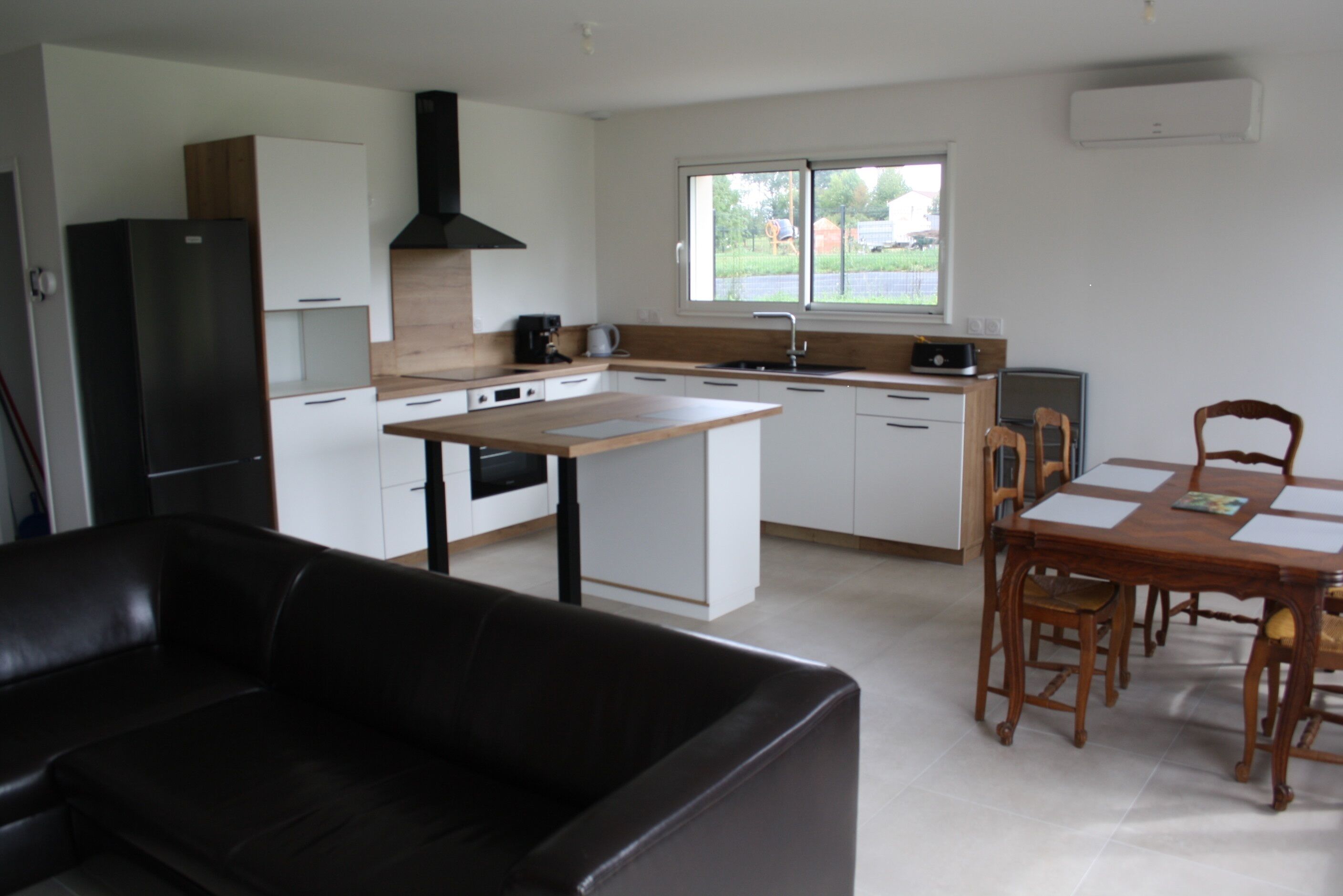 Een moderne keuken met een centraal eiland, een eethoek met tafel en stoelen, en een zwarte leren bank.