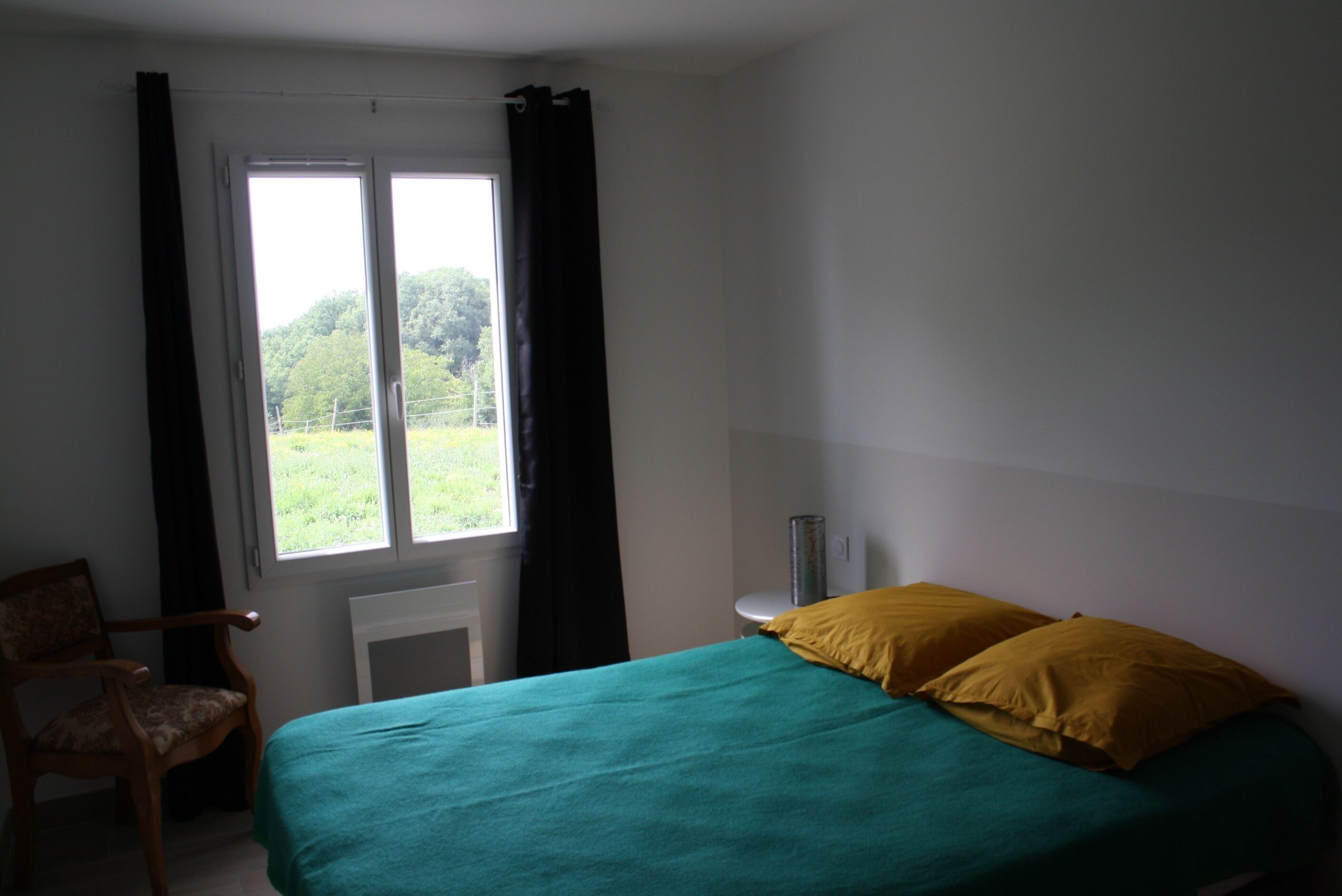 A bedroom with a bed, a chair, a window with curtains, and a radiator.