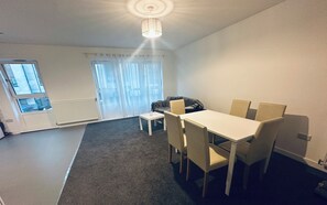 Ein Essbereich mit Tisch und Stühlen, einem kleinen Beistelltisch, einer Couch und einem Fenster mit Vorhängen.