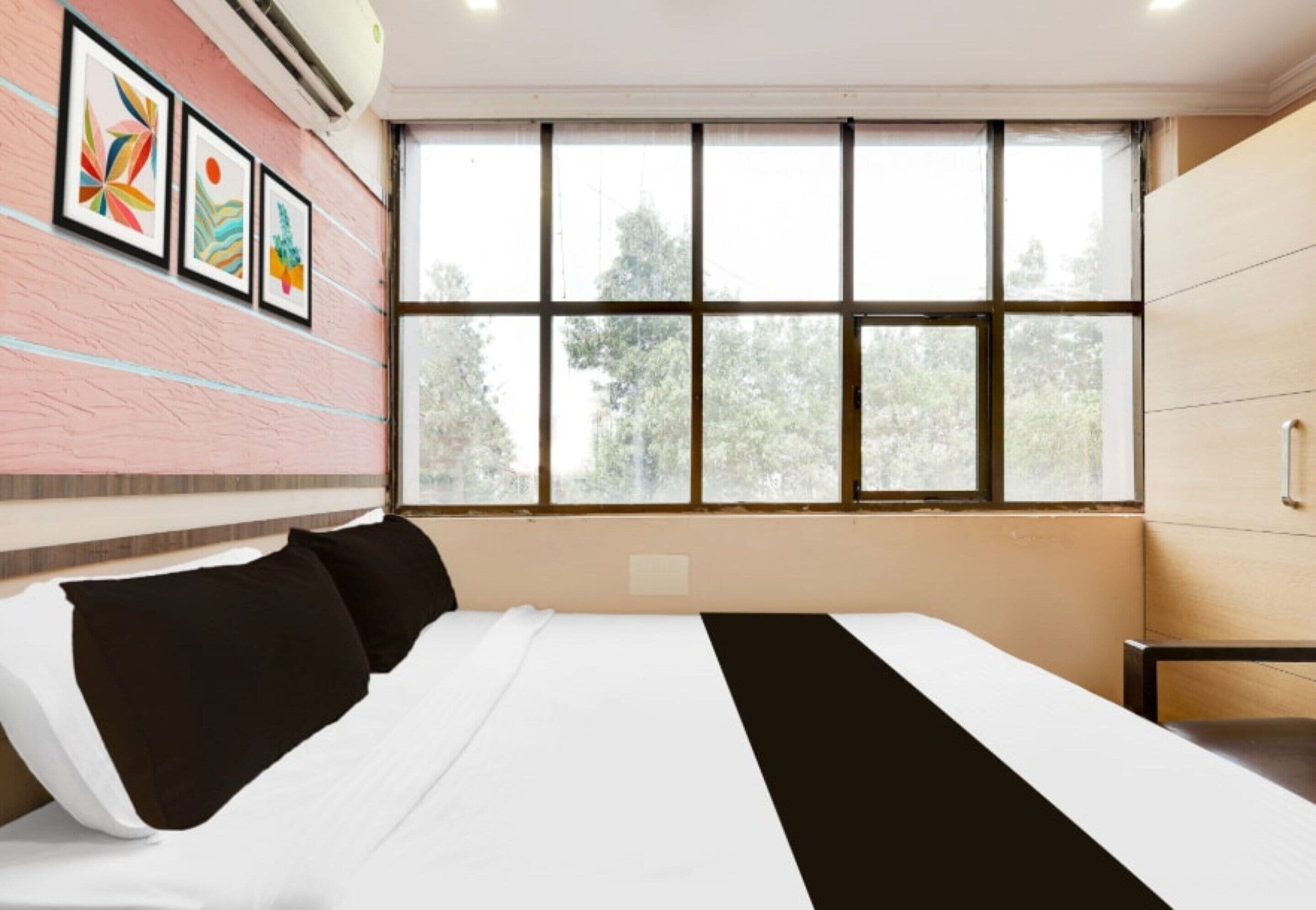 Una habitación de hotel con un ventanal grande, una cama con ropa de cama blanco y negro, y una pared de ladrillo con obras de arte enmarcadas.