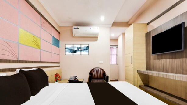 Ein Hotelzimmer mit Bett, Fernseher, Sessel, kleinem Tisch und Wand mit farbigem abstrakten Muster.