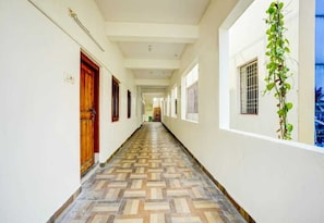 A hallway with patterned flooring, wooden doors, and a plant on the right wall. - Classic Gajuwaka (Visakhapatnam)
