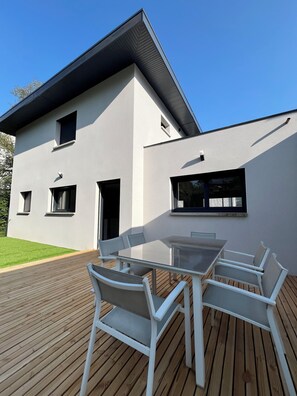 A modern house with a flat roof, a wooden deck, and a dining area with white furniture. - Villa Nova Annecy | Downtown & Lake | Sleeps 8 (Annecy)