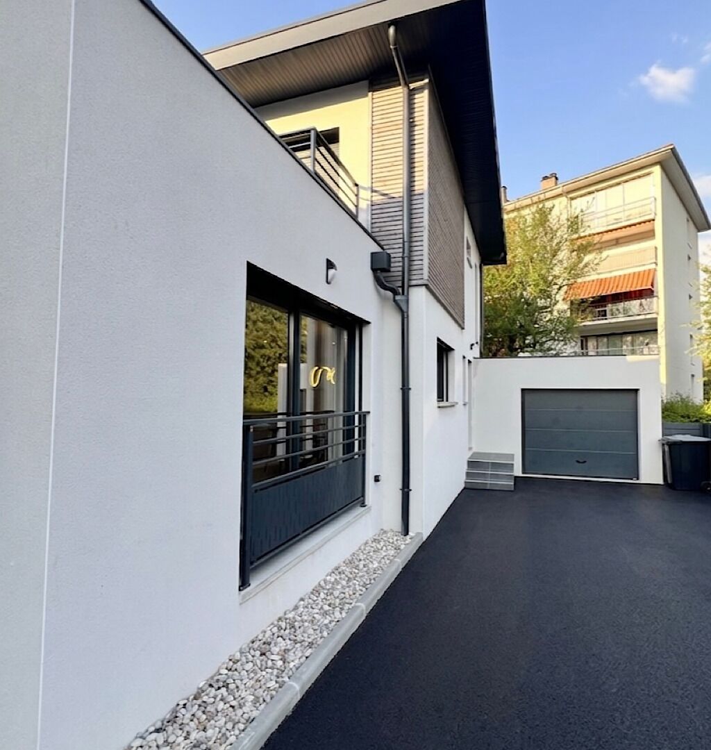 A modern building with a garage door, a balcony, and a pathway leading to the entrance.