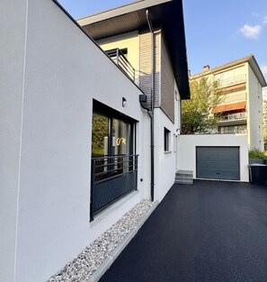 Um edifício moderno com porta de garagem, varanda e um caminho que leva à entrada.