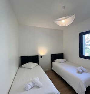 Habitación pequeña y limpia con dos camas individuales, una lámpara en la pared y una ventana.