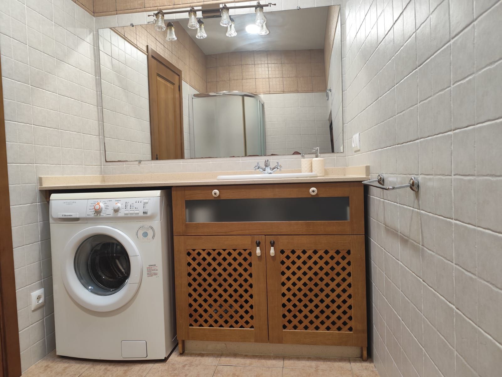 A compact bathroom with a washing machine, a sink, and a mirror.