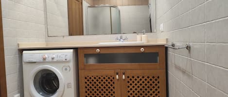 A compact bathroom with a washing machine, a sink, and a mirror.